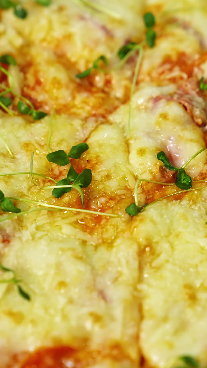 Delicious pizza. Melted cheese and green sprouts on pizza. Appetizing pizza spinning on the table. Close-up. Vertical video