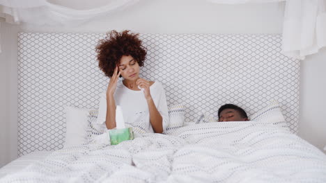 couple in bed with woman ill and suffering with symptoms of cold