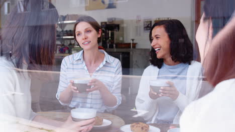 female friends talking at a coffee shop, seen through window