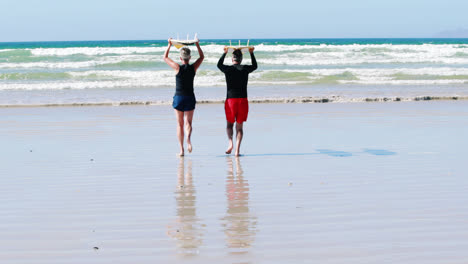 Pareja-Mayor-Llevando-Tabla-De-Surf-Sobre-La-Cabeza-Mientras-Corre-Hacia-El-Mar