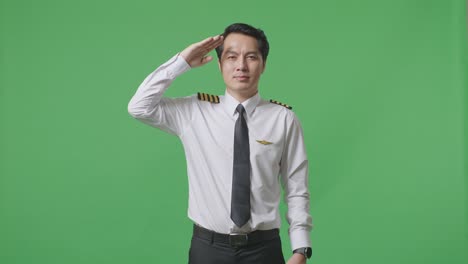 asian man pilot is respectful, saluting while standing in the green screen background studio