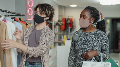 stylist in face mask helping african american woman in clothes shop