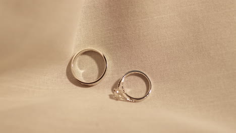 close-up of two platinum and diamond engagement rings falling over each other as they are placed on a cream colored cloth