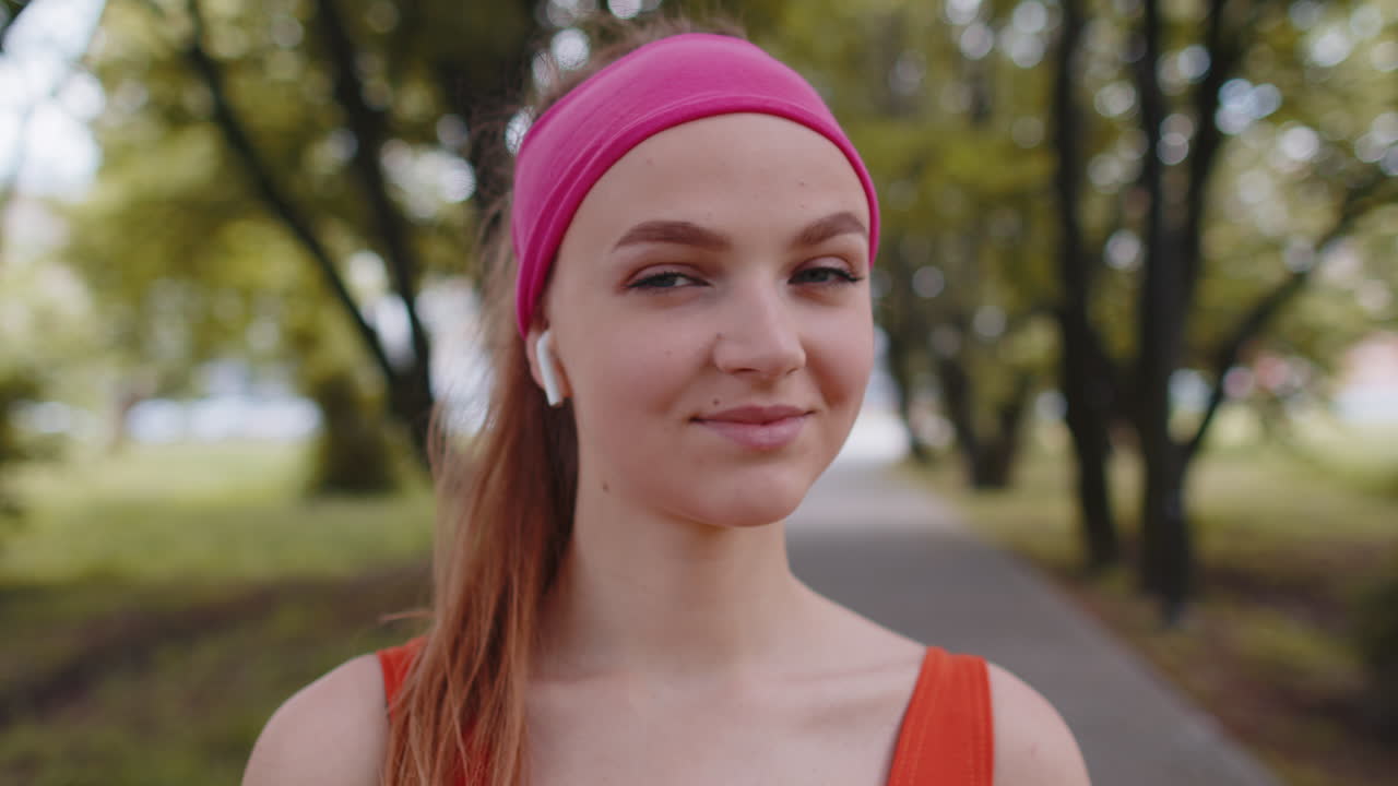 Porträtt av en atletisk löparflicka som tränar och lyssnar på sin favoritlåt i hörlurar i parken.