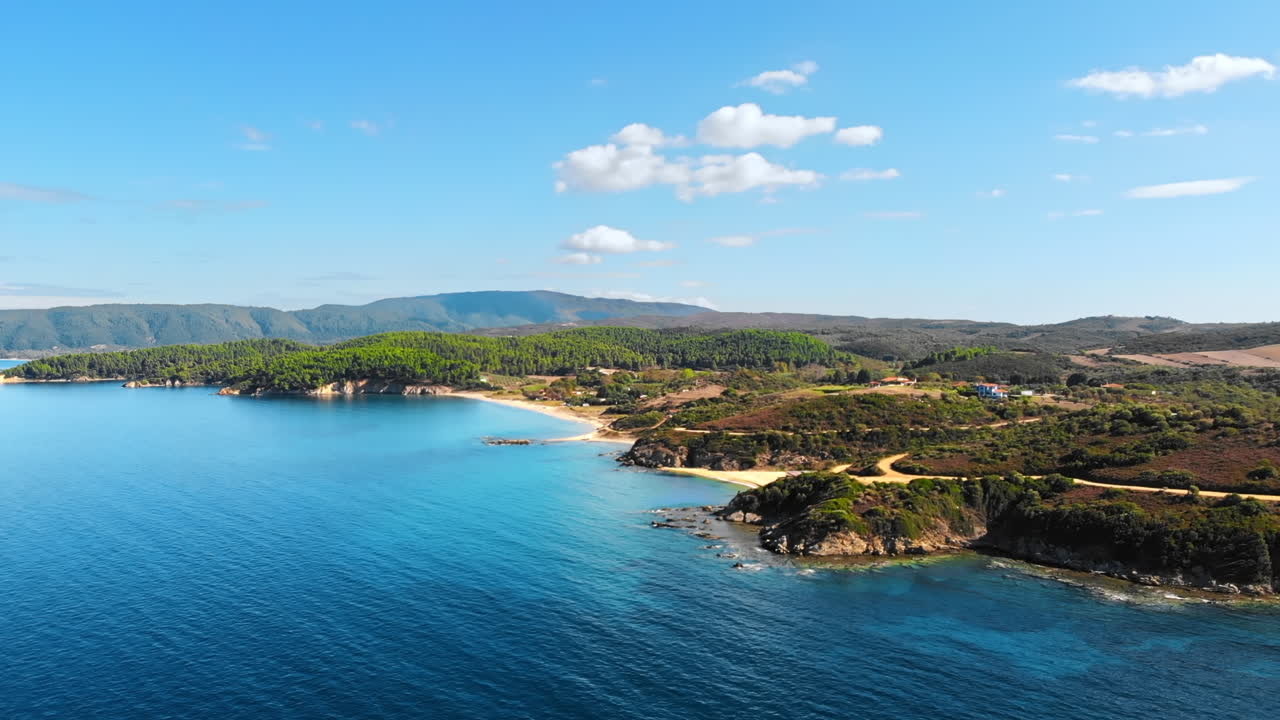 Aerial drone view of the Aegean sea rocky coast with greenery and beaches along the shore and hills in the distance, blue water in Greece