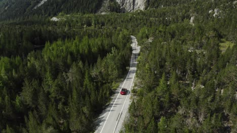 aerial view red car driving through a valley surrounded by mountains