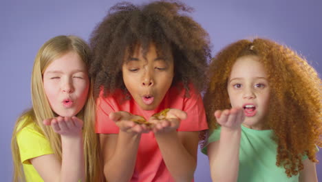 studio shot of children blowing glitter from hands on purple background