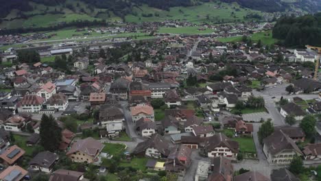 Cámara-De-Drones-Que-Pasa-Por-Encima-De-Edificios-Altos-Y-Bajos.-Muchos-Vehículos-De-Cuatro-Ruedas-Y-Bicicletas-Recorren-La-Carretera-Entre-Los-Edificios.