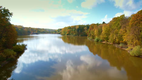 sunny day footage over the river flowing between foresty banks. drone flying along the water flow closer to road and some country houses.
