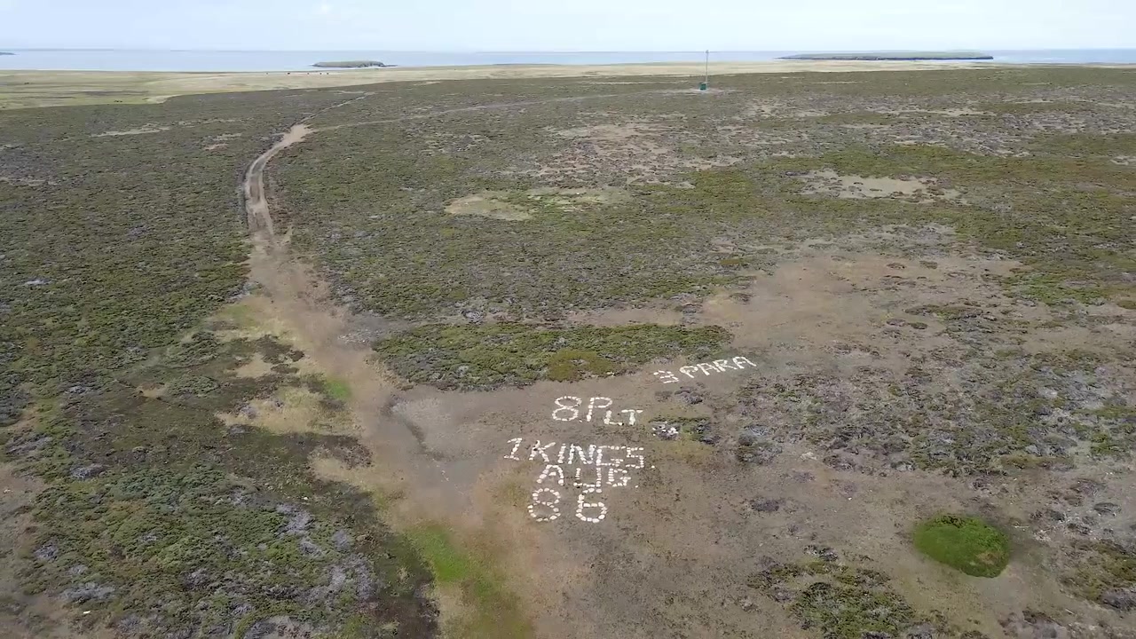 El movimiento de la cámara captura una vista hacia atrás sobre un campo, revelando un mensaje hecho de piedras blancas