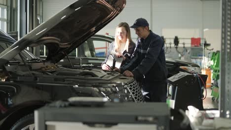 gerente femenina discutiendo la reparación de vehículos con el mecánico en el taller de reparación de automóviles