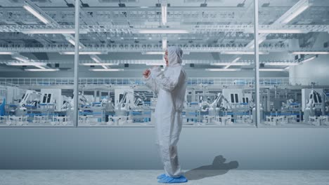 vista lateral del cuerpo completo del científico masculino asiático celebrando el éxito mientras está de pie en una fábrica de laboratorio moderna con robots automatizados