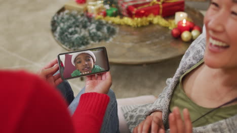pareja asiática sonriente usando un teléfono inteligente para una videollamada de navidad con un niño con sombrero de papá noel en la pantalla