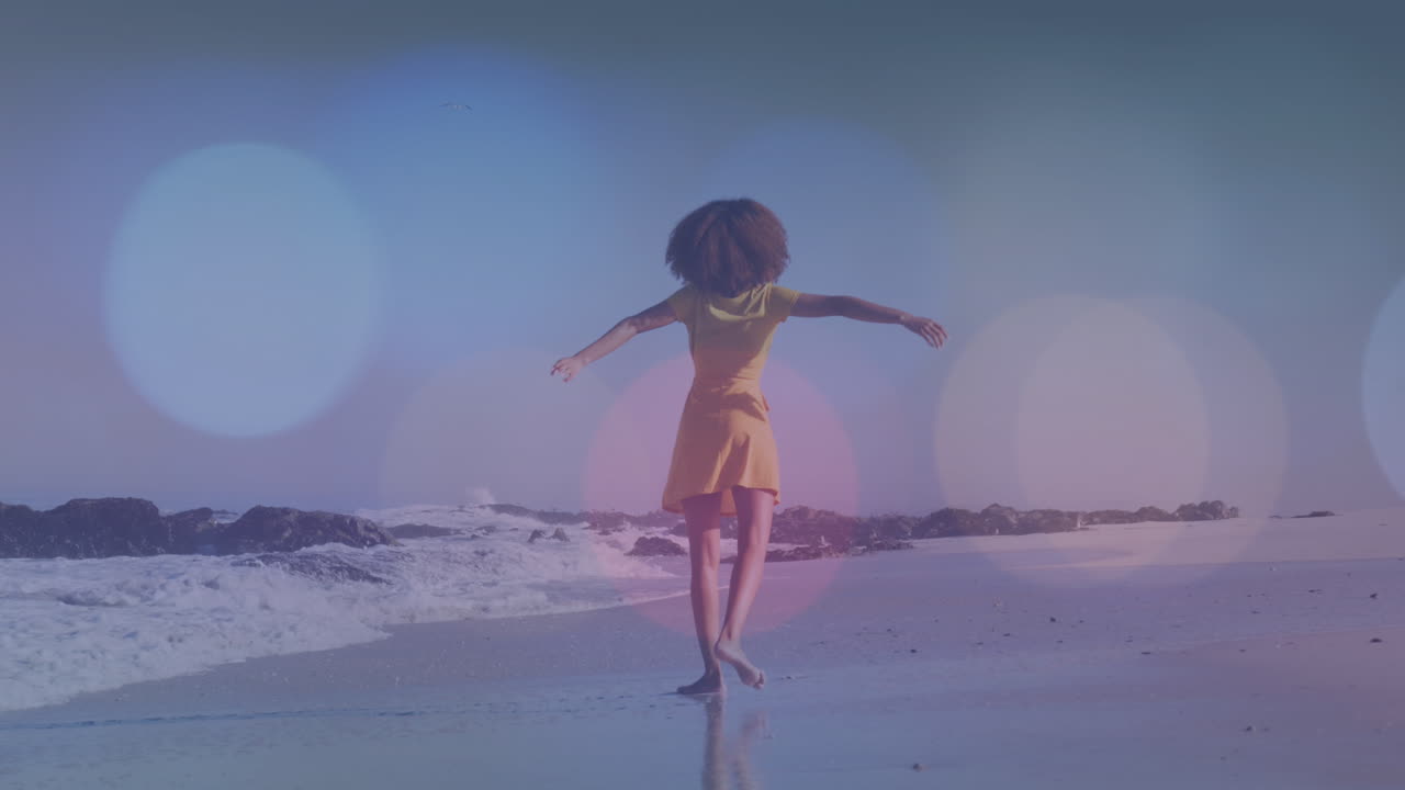 Animation von Lichtpunkten über einer afroamerikanischen Frau, die am Strand tanzt