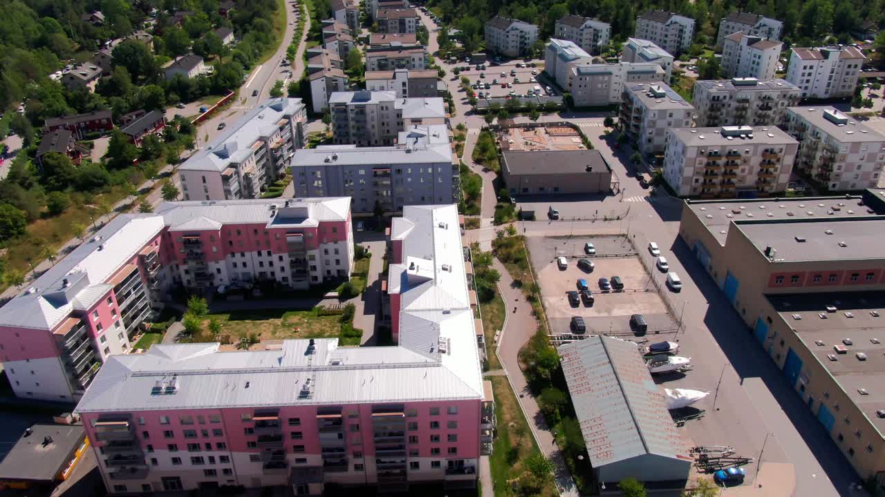 Vista aerea dall'alto di palazzi rosa e bianchi con parco giochi interno nel cortile e parcheggio nel sobborgo di Gustavsberg. Rappresenta lo stile di vita svedese contemporaneo