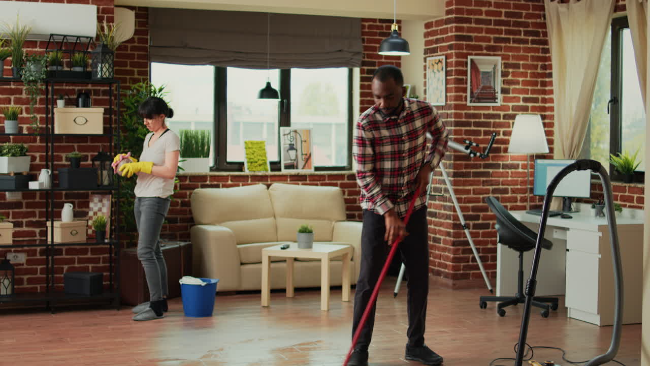 Young couple cleaning living room with vacuum and furniture polish