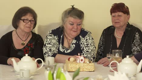mujer mayor con amigas sentadas alrededor de la mesa de cena con pastel de cumpleaños