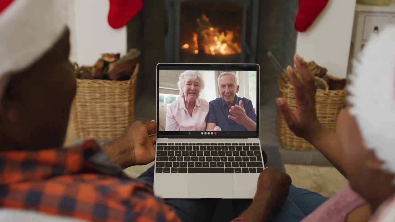 pareja afroamericana con sombreros de santa usando una computadora portátil para una videollamada de navidad con la pareja en la pantalla