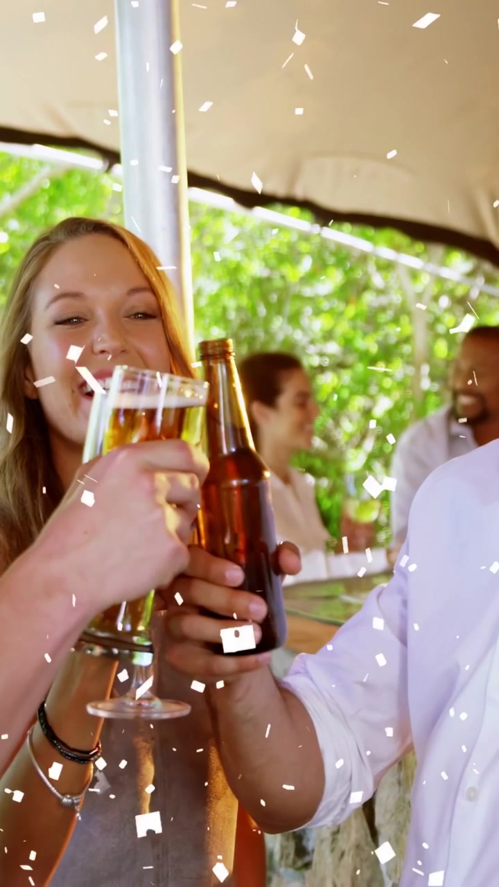 Vertical video: Confetti falling as woman lifting wine glass and man clinking beer, celebrating