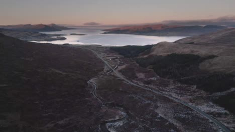 Paisaje-Escarpado-De-La-Isla-De-Skye-Al-Atardecer-Con-Caminos-Sinuosos-Y-Un-Sereno-Lago-Marino,-Vista-Aérea