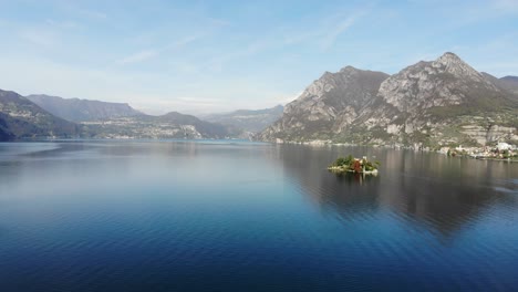 Drone-Vuela-Lentamente-Desde-Monte-Isola-A-La-Isla-De-Loreto-En-El-Lago-Iseo-Durante-Un-Soleado-Día-De-Otoño