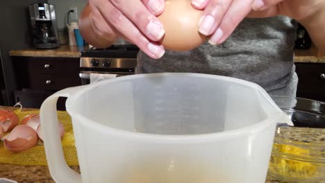 anonymous female hands cracking eggs into plastic jug preparing for cooking in kitchen
