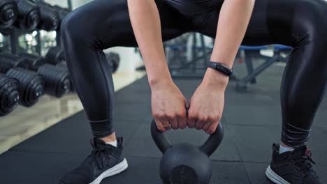 sporty female lifting kettlebell. athlete woman wearing black leggings and trainers training with hard weight in sports club. close-up.