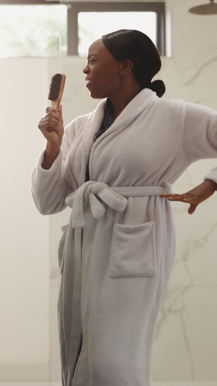 Young Woman in Bathrobe Singing and Dancing with Hairbrush in Bathroom