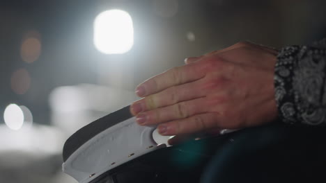 close up of individual hand gently resting on black skating boot under bright light during winter night with soft background bokeh and subtle lens flare adding atmosphere to the outdoor cold scene