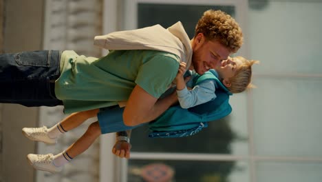 vertical video a little boy in blue clothes with a blue backpack runs after school to his father in a green t-shirt with curly hair. happy meeting of father parent and his little boy after school