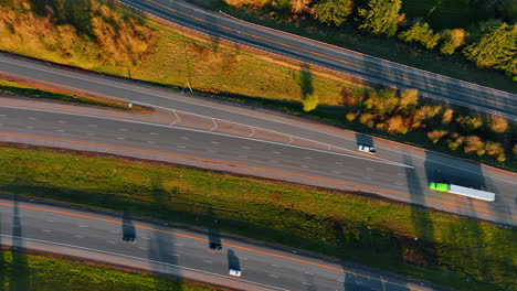 Highways divided by the green grass. Cars go quickly by the roads. Top view on the motorway at sunset.