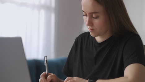 home-education-of-student-or-high-schooler-teen-girl-is-viewing-online-lecture-on-laptop-and-writing-homework-medium-portrait-in-living-room