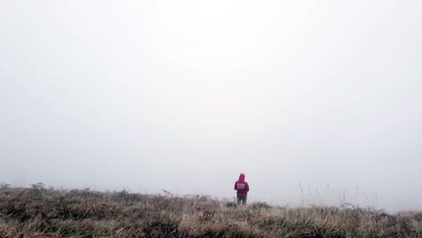 Drohnenvideo-Eines-Mannes,-Der-Einen-Kapuzenpulli-Trägt-Und-An-Einem-Sehr-Bewölkten-Tag-Auf-Den-Boden-Blickt,-Symbolisiert-Depression,-Traurigkeit-Und-Einsamkeit,-Der-Blick-Auf-Das-Passieren-Von-Schuss-Warf-Tote-Alte-Pflanzen,-Was-Das-Dunkle-Gefühl-Verstärkt