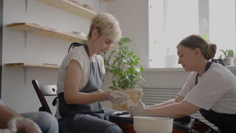 A female potter&#039;s wheel sculpting teacher explains how to work and teaches an elderly woman to work with clay and make mugs and jugs. Master class for pensioners. Pottery courses