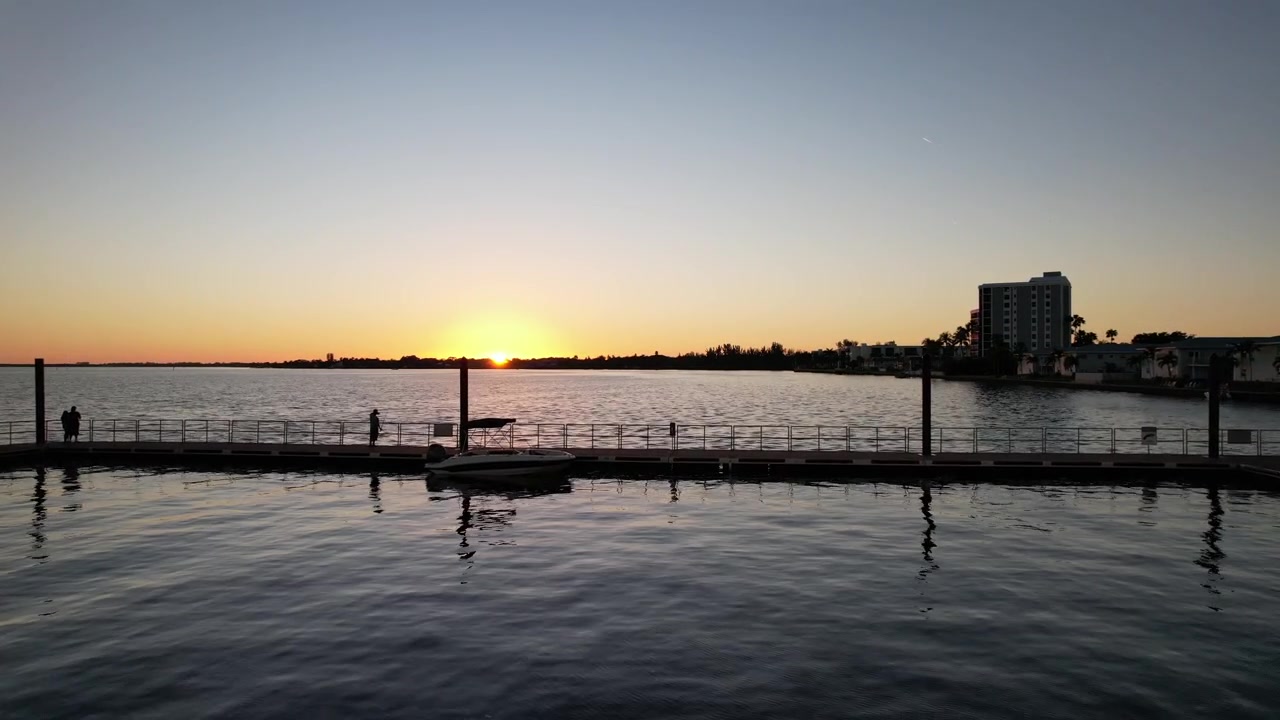 On the shore next to the city, reflecting the bright sunlight, there is a wonderful panoramic view of the sunset over the smooth water surface.