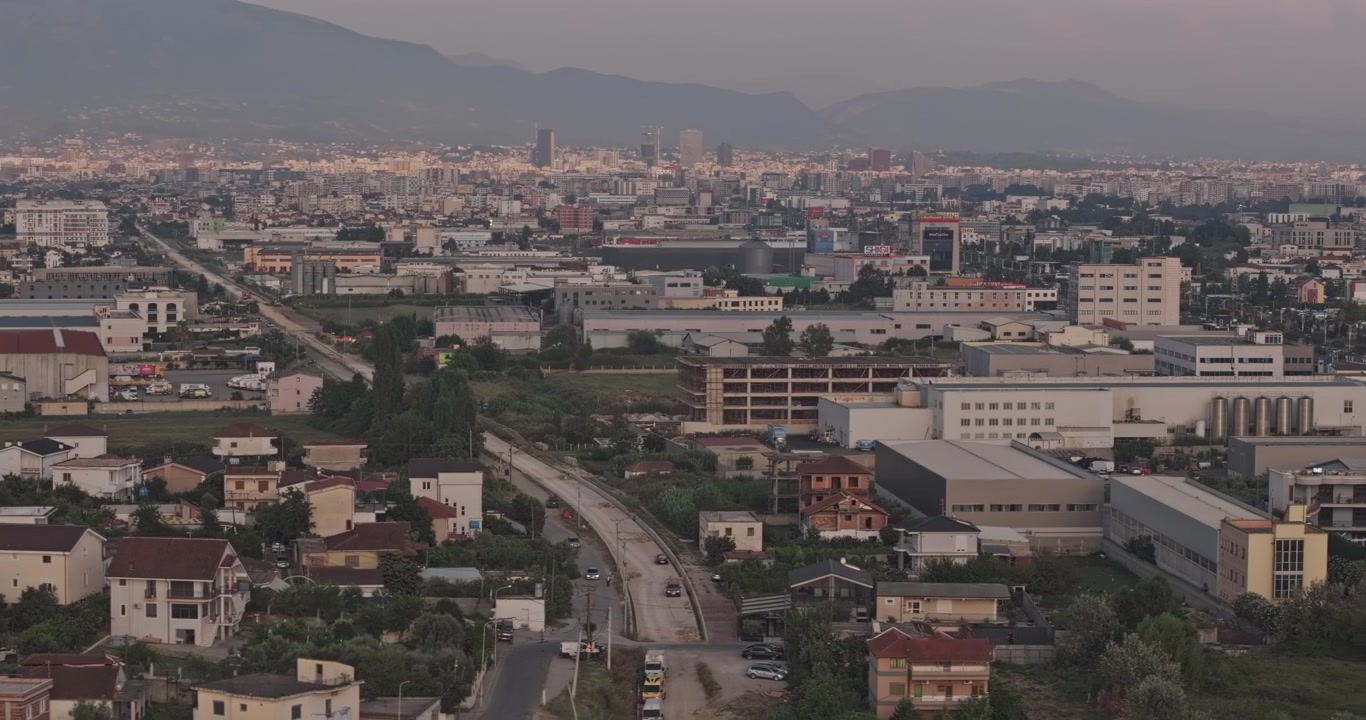Tirana, Albania. Sobrevuelo aéreo bajo con teleobjetivo v8 sobre Domje, capturando densos suburbios residenciales, edificios comerciales y el centro de la ciudad distante al atardecer. Filmado con Mavic 3 Pro Cine - 20 de julio de 2024