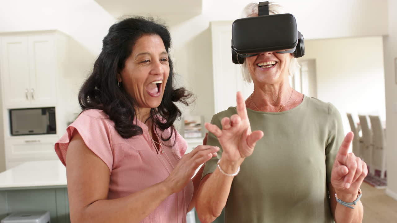 Donne anziane felici e di diverse etnie che usano occhiali VR e ridono in soggiorno soleggiato, al rallentatore