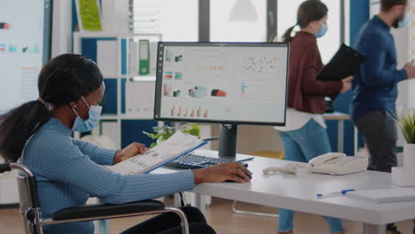 Black-woman-with-disabilities-and-protection-face-masks-working-on-computer