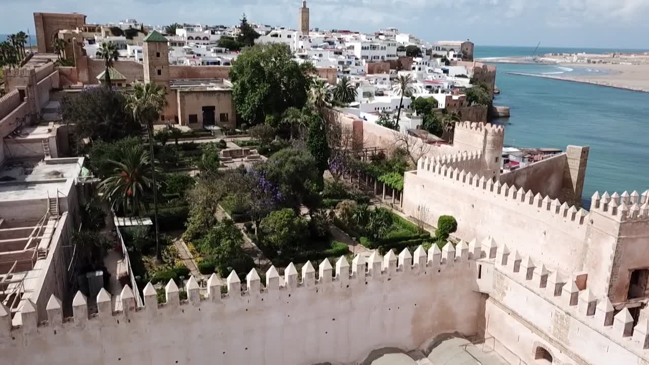 Naturskøn droneoptagelse over de befæstede mure i Kasbah of the Udayas. Afslører de frodige andalusiske haver indeni, omgivet af traditionelle hvide huse og havhorisonten i Rabat.