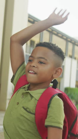 video of happy african american boy waving to colleagues in front of school