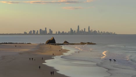 people walking and surfing at currumbin beach on sunset - currumbin alley and surfers paradise high rise buildings - view from the elephant rock lookout - gold coast, qld, australia