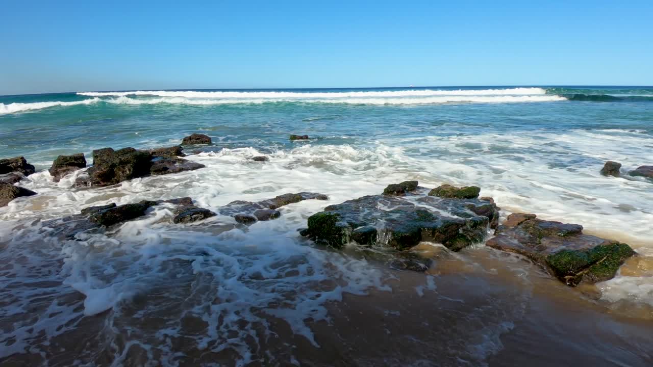 olas rodando sobre rocas ubicadas en una playa de arena en sydney