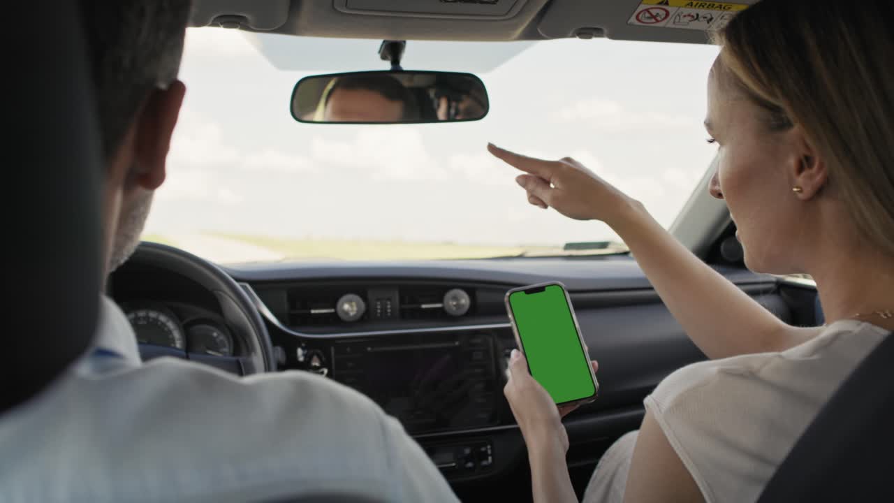 vista trasera de una pareja caucásica de mediana edad conduciendo un coche y usando un mapa en un teléfono inteligente.
