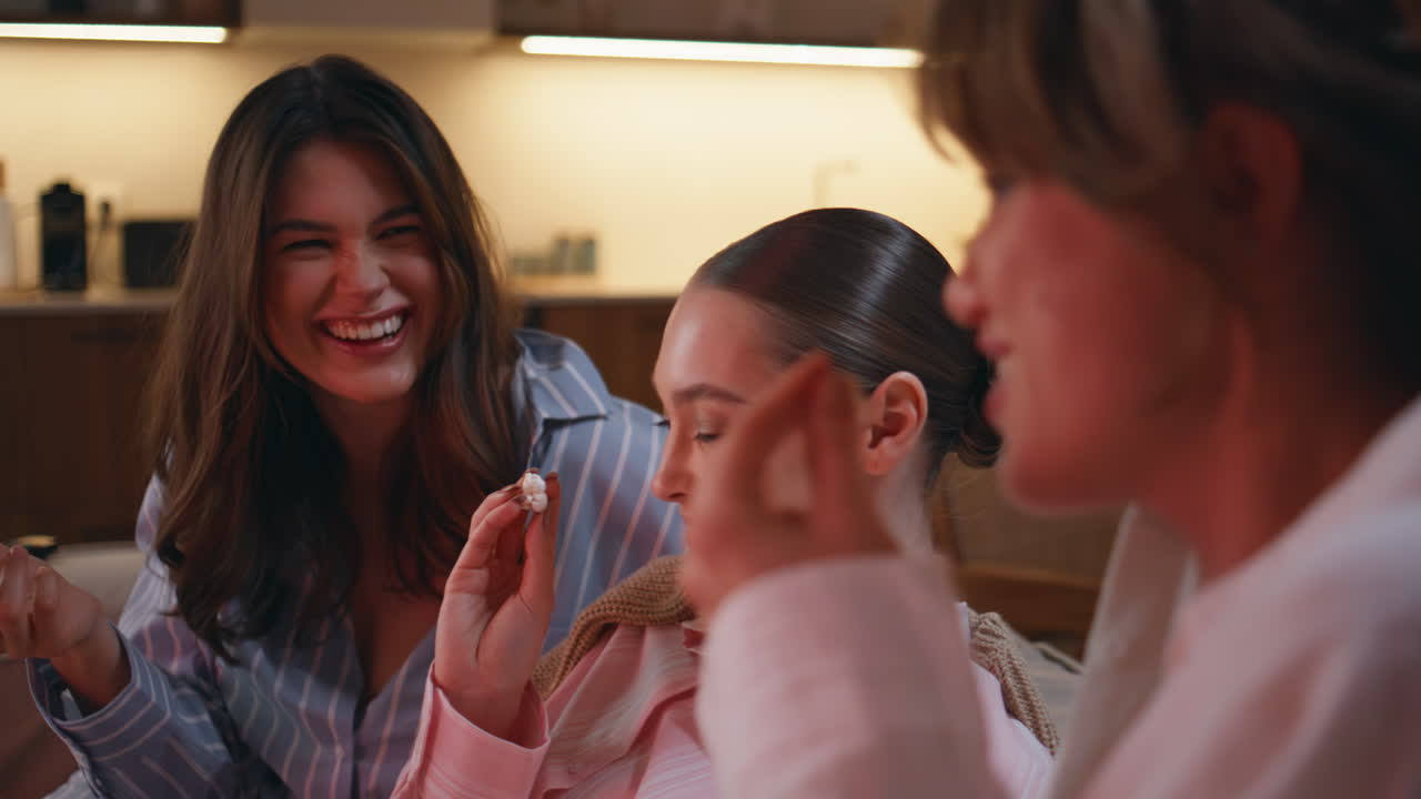 Three friends eating popcorn watching movie at pajamas party home closeup