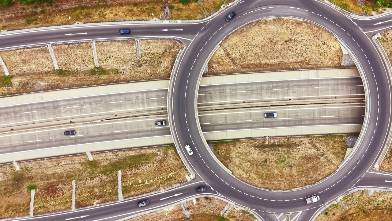 Traffic flows on a roundabout connecting two major roads in a rural area during daytime