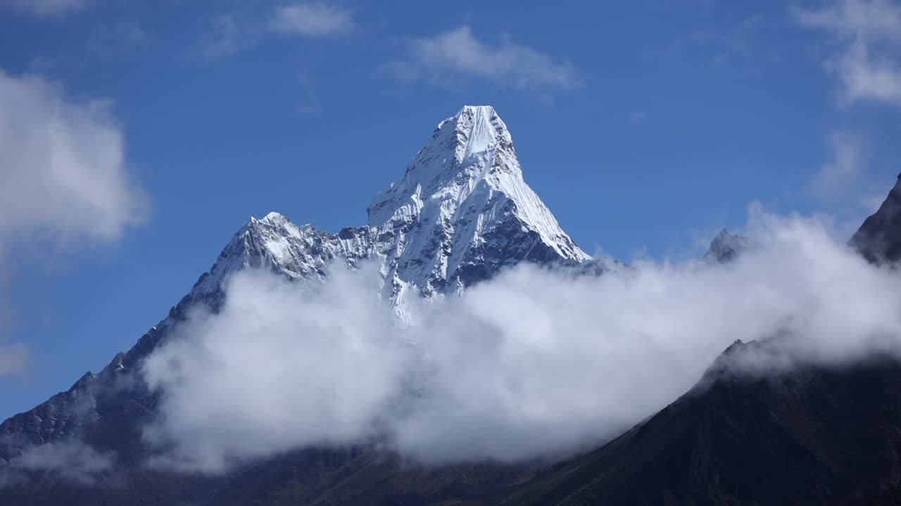 Majestic view of Ama Dablam Mountain in Nepal, its sharp snow-covered summit emerging above drifting clouds against a clear blue sky in the Himalayan range
