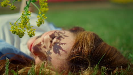 Relaxed-girl-posing-with-wild-flower-in-green-park.-Branch-shadow-on-pretty-face