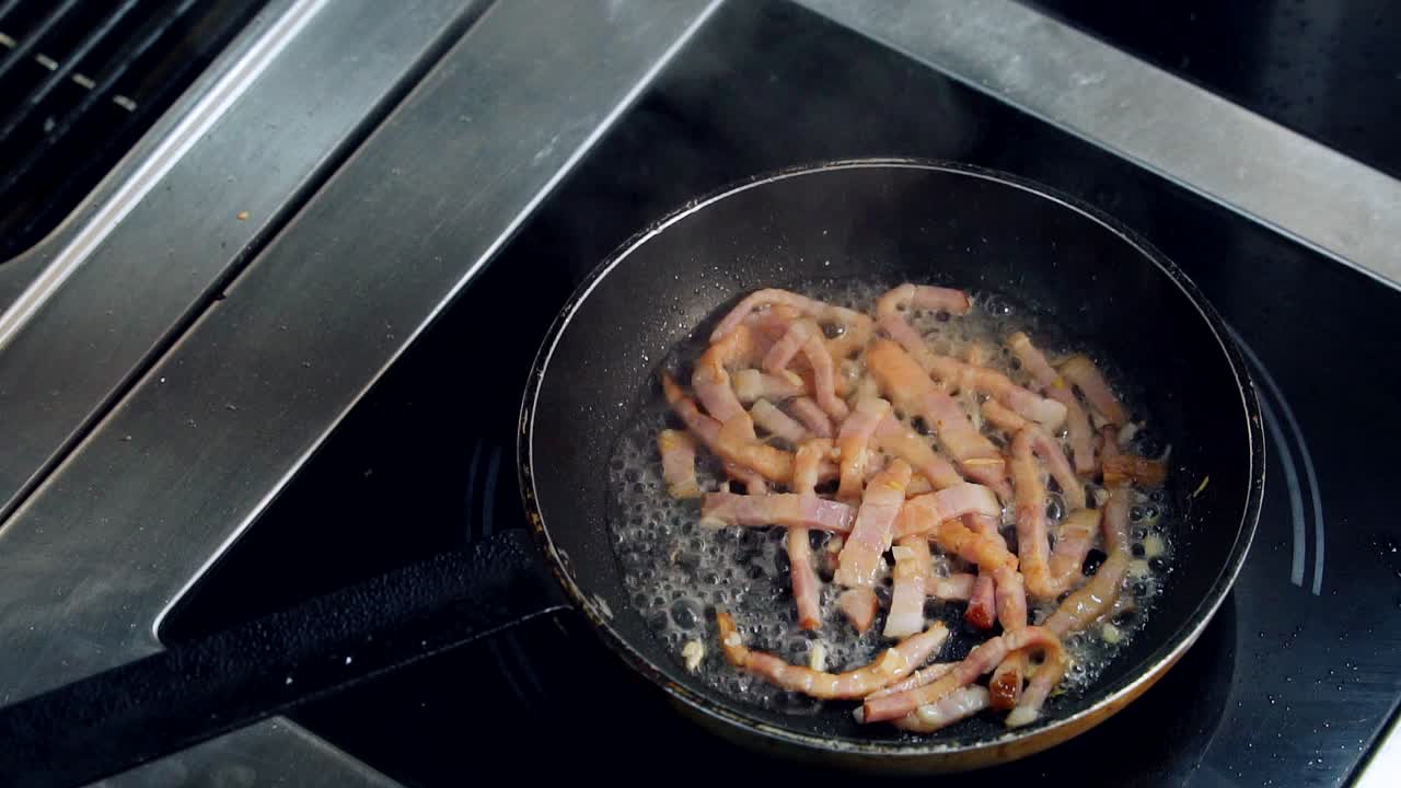 Cooking delicious breakfast on a frying pan. Amazing bacon frying in fat, sizzling and smoking in a hot pan. Top view