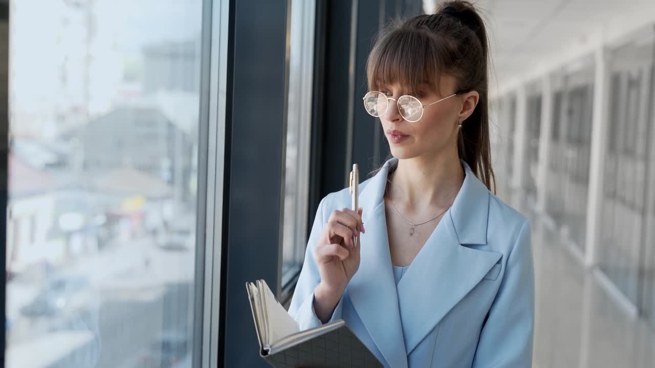 hermosa joven con gafas y un elegante traje con un diario escribe con un bolígrafo y piensa