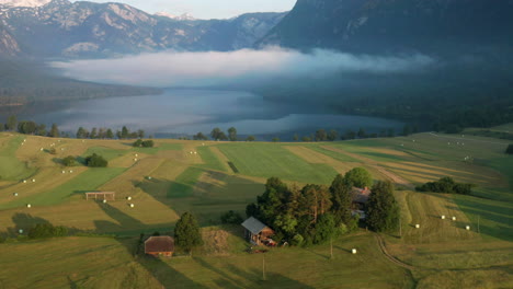 clouds and fog over lake bohinj from countryside fields with hay bales at sunrise in slovenia